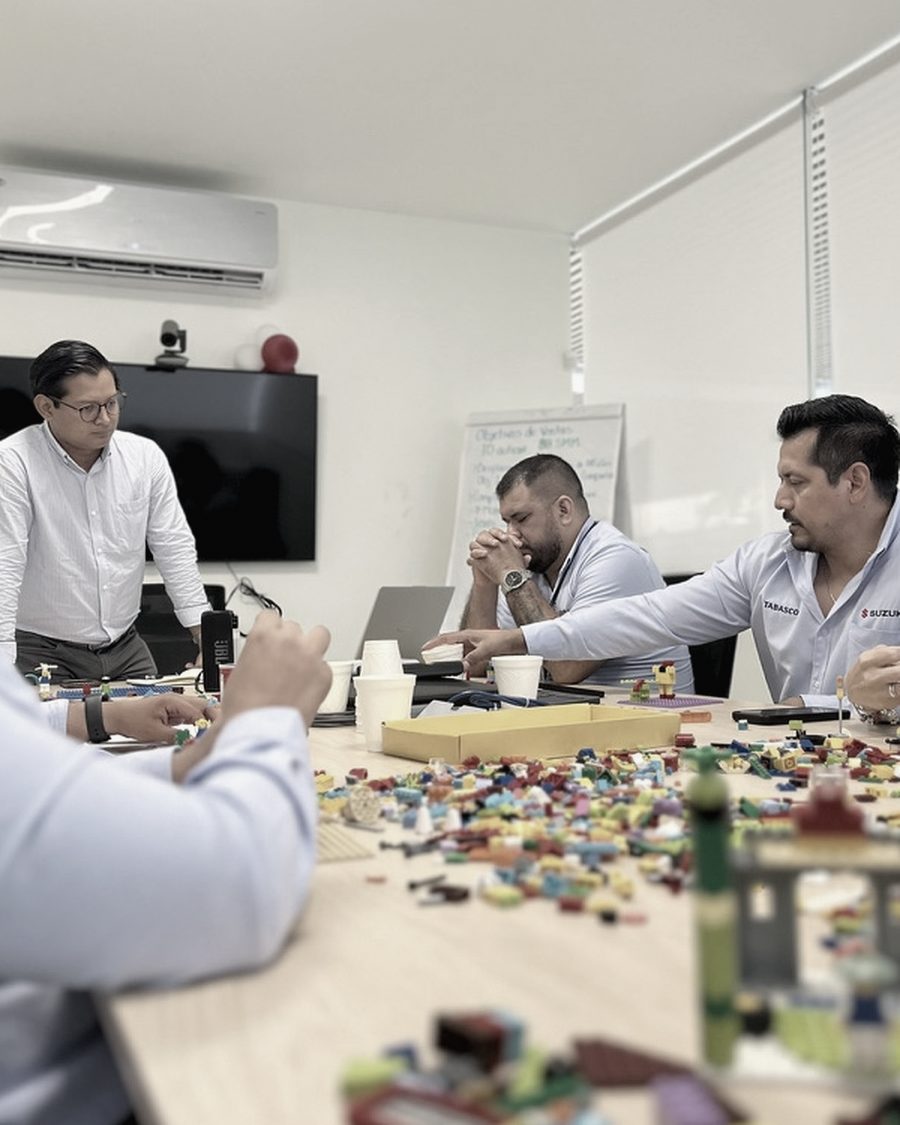 Equipo de Suzuki México durante una sesión de integración: el facilitador de pie y cuatro participantes trabajando sobre la mesa.